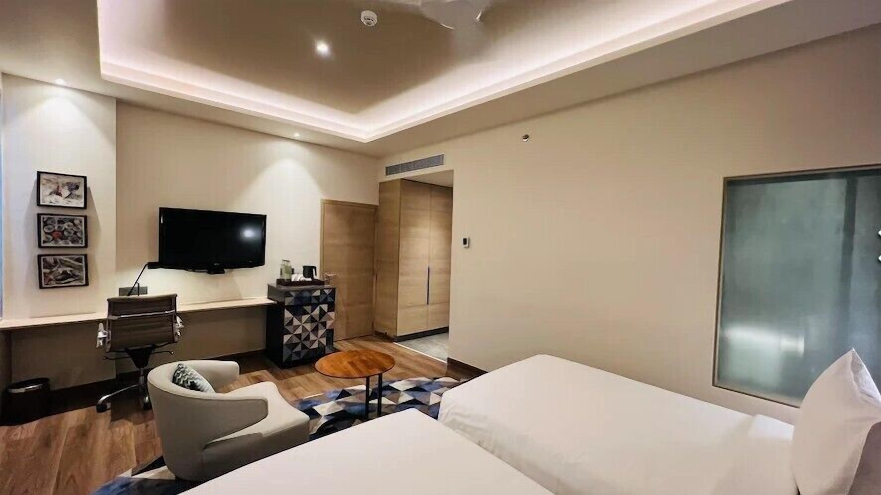 Een moderne hotelkamer met een bed, een bureau, een stoel, een televisie en kunst aan de muur.