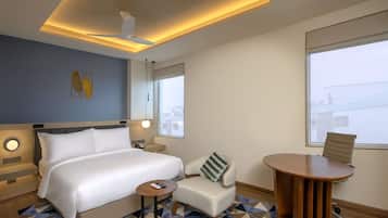 A modern hotel room with a large bed, a small sofa, a round wooden table, and a view of the city through the window.