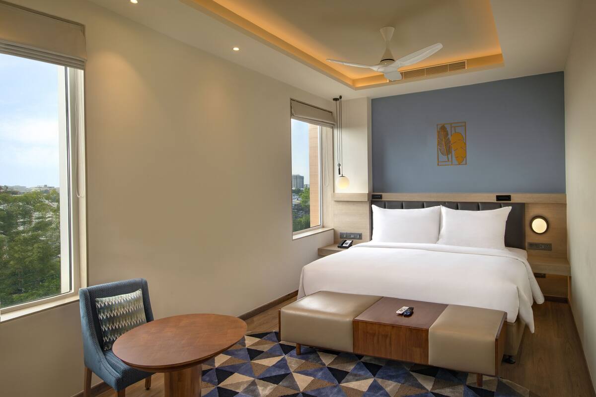 A hotel room with a bed, a desk, a chair, a window, and a ceiling fan.