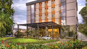 A modern multi-story hotel with a covered entrance, surrounded by a well-maintained garden with colorful flowers. - O by Tamara Coimbatore (Coimbatore)