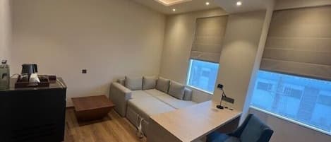 A modern, compact room with a built-in desk and chair, a sofa, and a small table with a coffee maker.