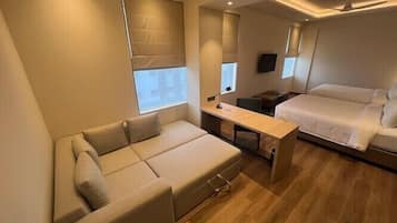 A modern, compact room with a sofa, a bed, a small table, and a TV.