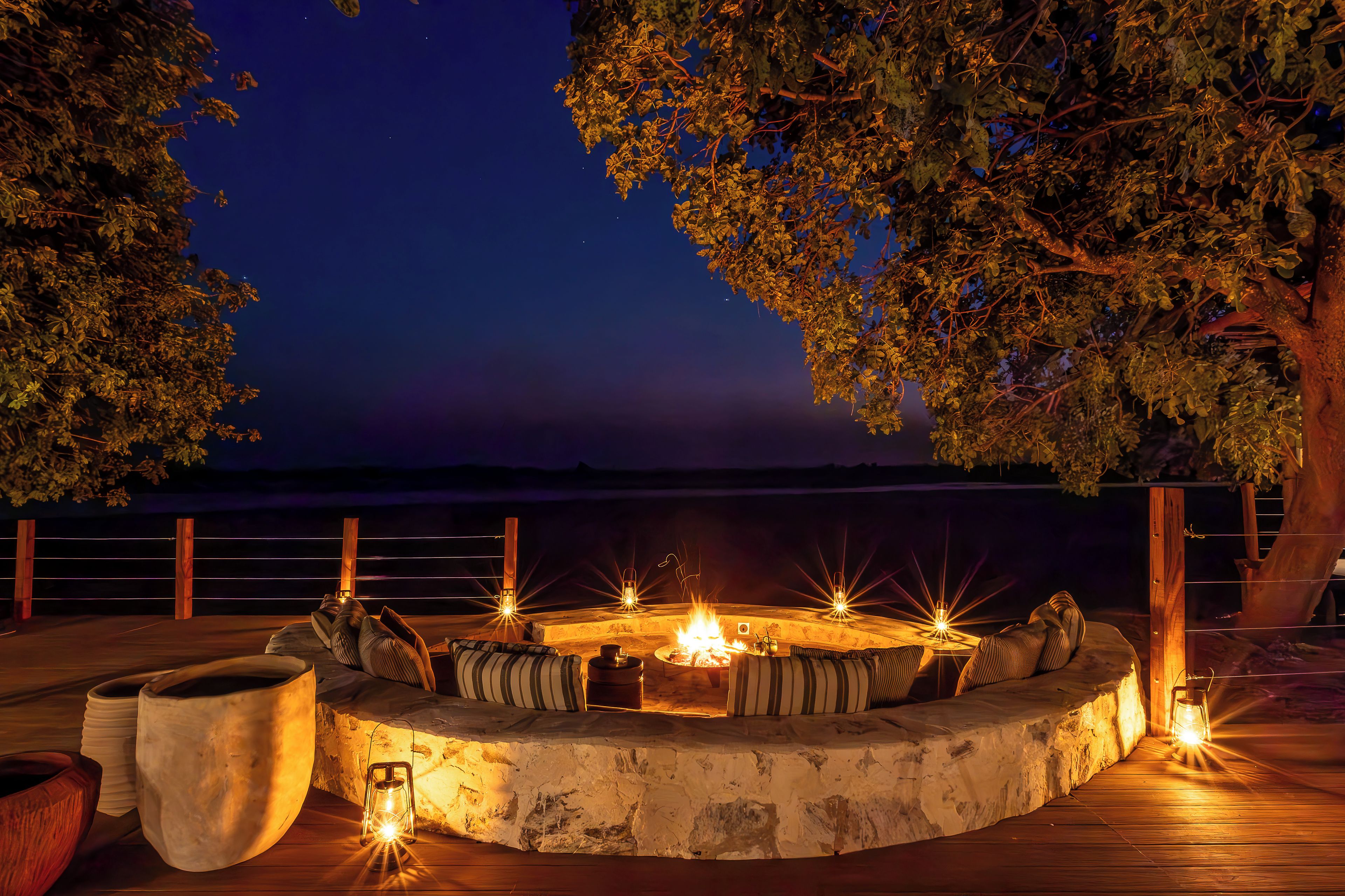 An outdoor seating area with a fire pit, surrounded by wooden railings and trees.