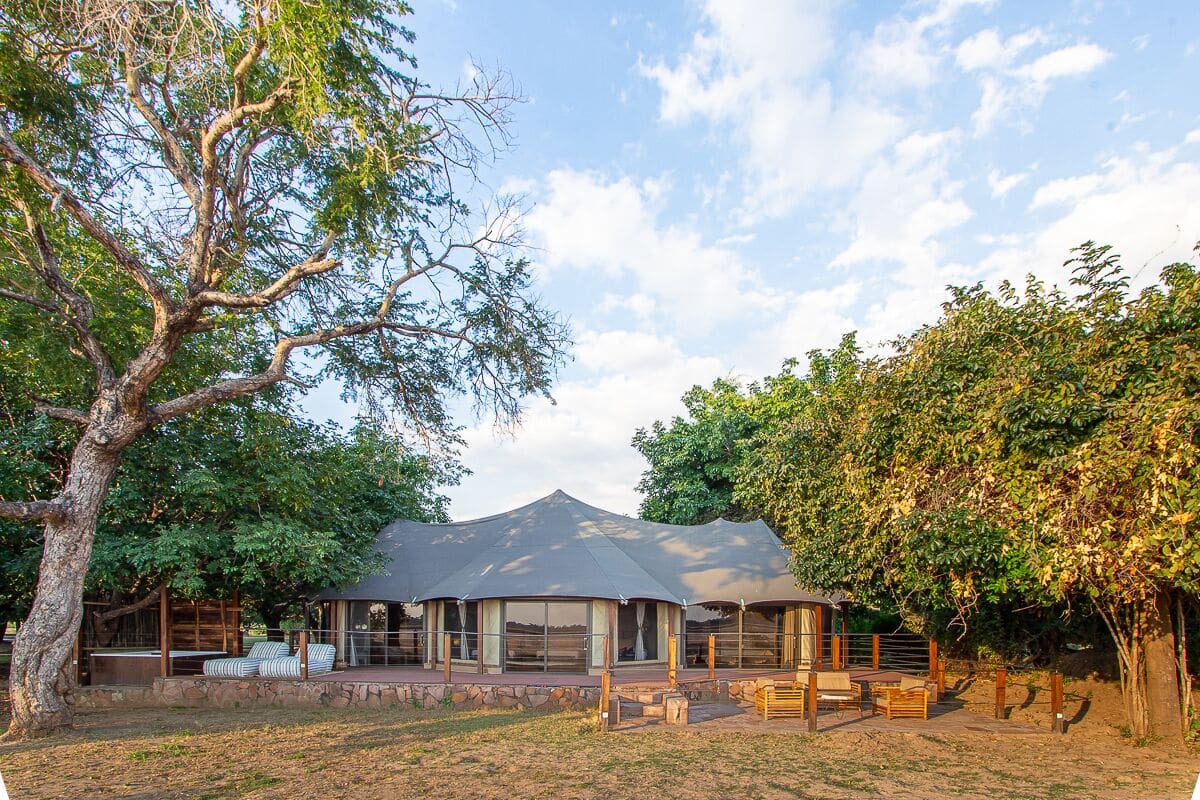 A large, open pavilion with a curved roof, surrounded by a stone wall and wooden fence.