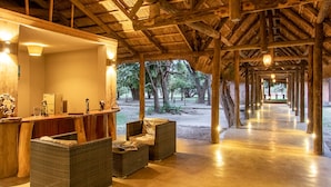 A covered outdoor area with a reception desk, wicker furniture, and a view of trees and a beach. - Mopani Safari Lodge (South Luangwa National Park)
