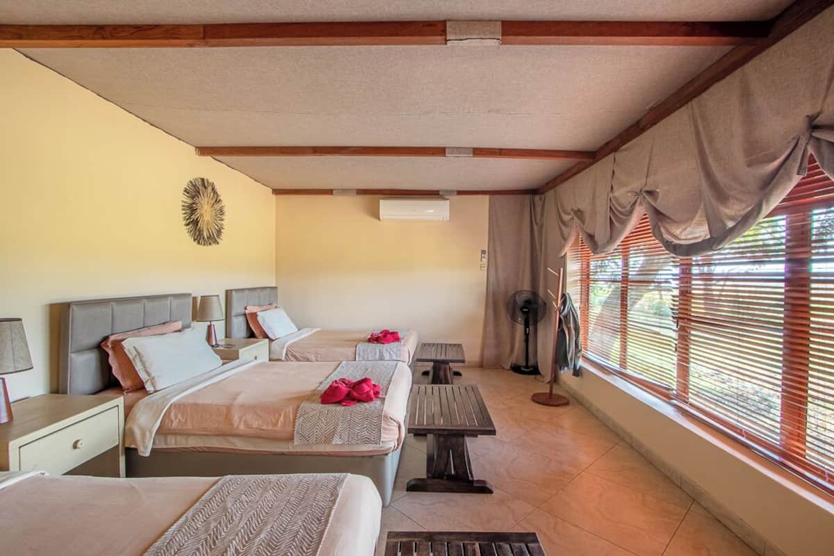 A hotel room with three beds, a fan, and a window with blinds.