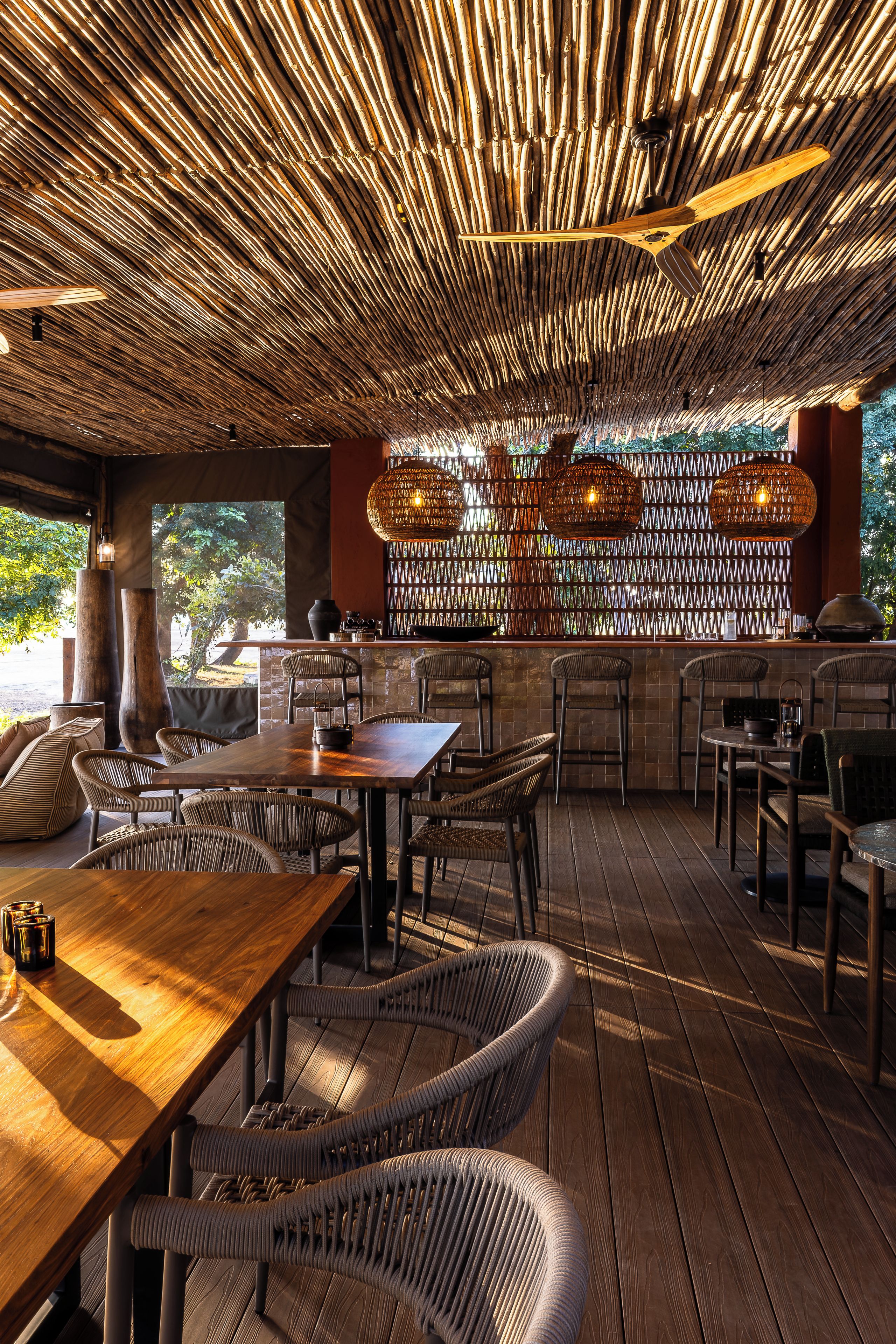 Un espacio de comedor al aire libre con techo de bambú, mobiliario de mimbre y pared de ladrillo con diseño trenzado.