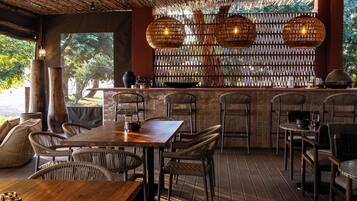 Un espacio de comedor al aire libre con techo de bambú, mobiliario de mimbre y pared de ladrillo con diseño trenzado.