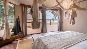 A bedroom with a large bed, a view of the outdoors, and a balcony with a railing. - Mopani Safari Lodge (South Luangwa National Park)