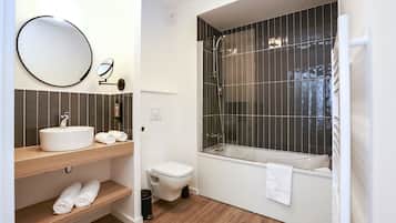 A modern bathroom with a round mirror, a white sink, a toilet, and a bathtub with a glass enclosure.