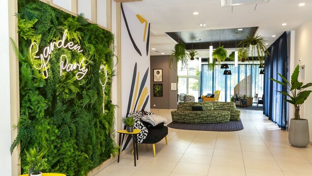 A modern hotel lobby with a green wall, a neon sign, and a seating area with patterned sofas. - Appart Hotel Odalys City Angers Centre Gare (Angers)