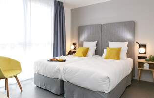 Una cama doble con ropa de cama blanca y amarilla, una mesita de noche con lámpara y una silla.
