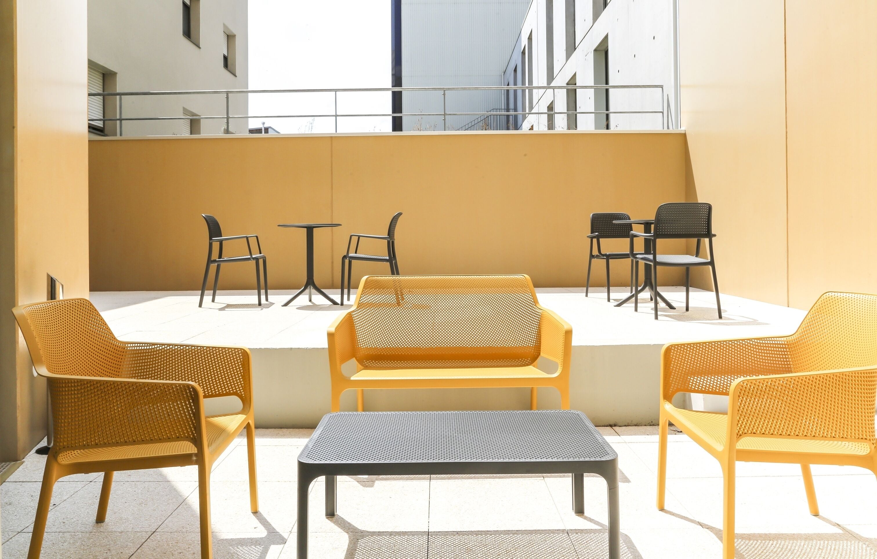 A terrace with yellow and black wicker furniture, including chairs and a table, set against a building facade.