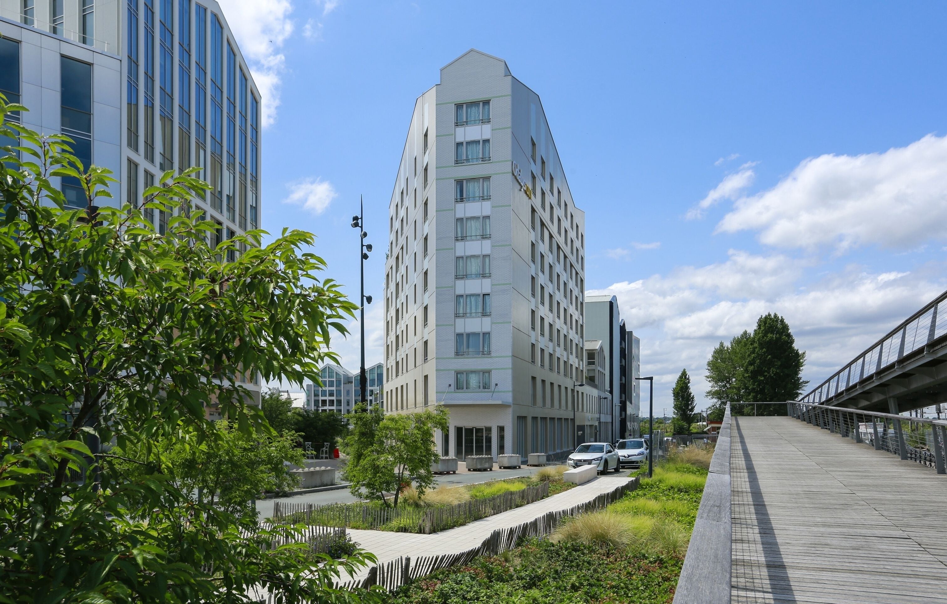A modern building with a unique angular design, surrounded by greenery and a pedestrian walkway.