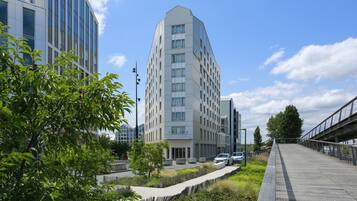 A modern building with a unique angular design, surrounded by greenery and a pedestrian walkway.