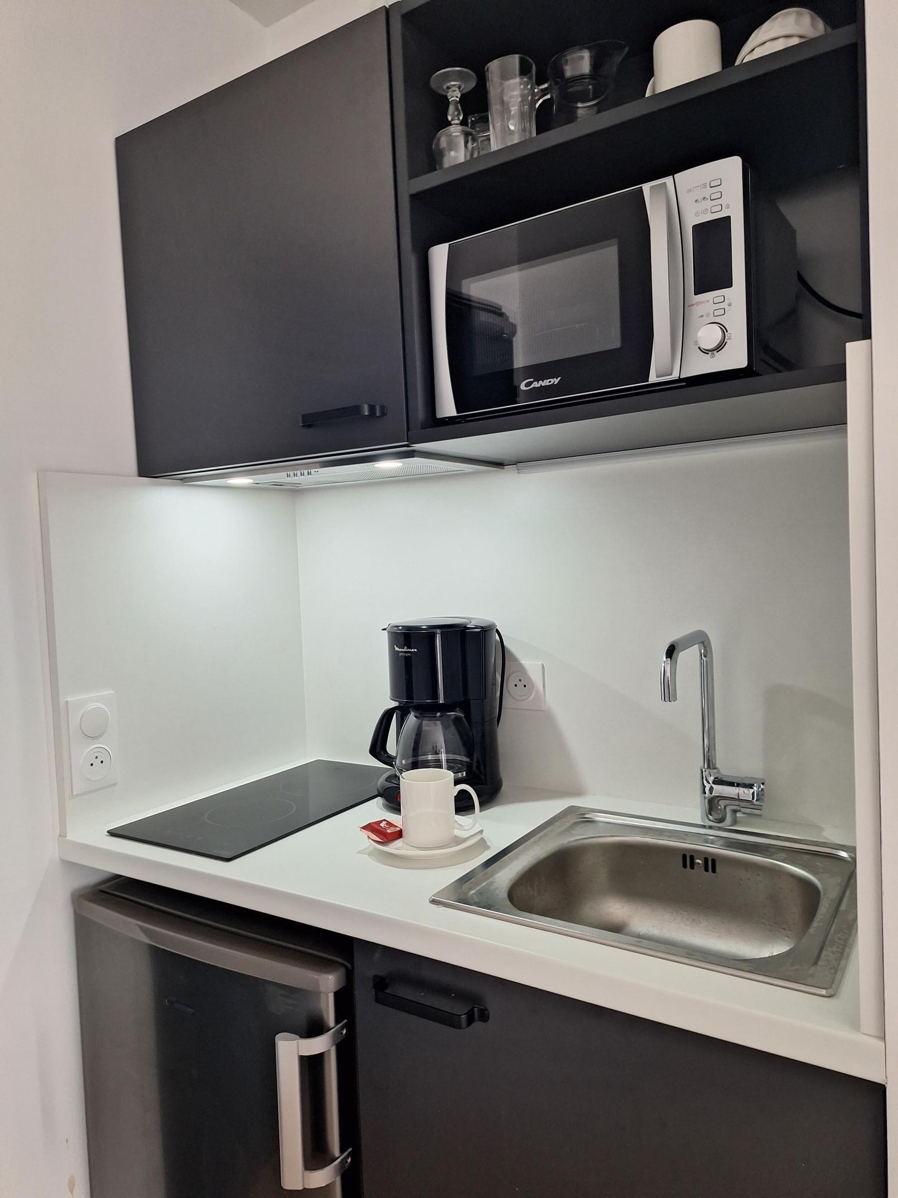 A compact kitchenette with a microwave, coffee maker, and sink.