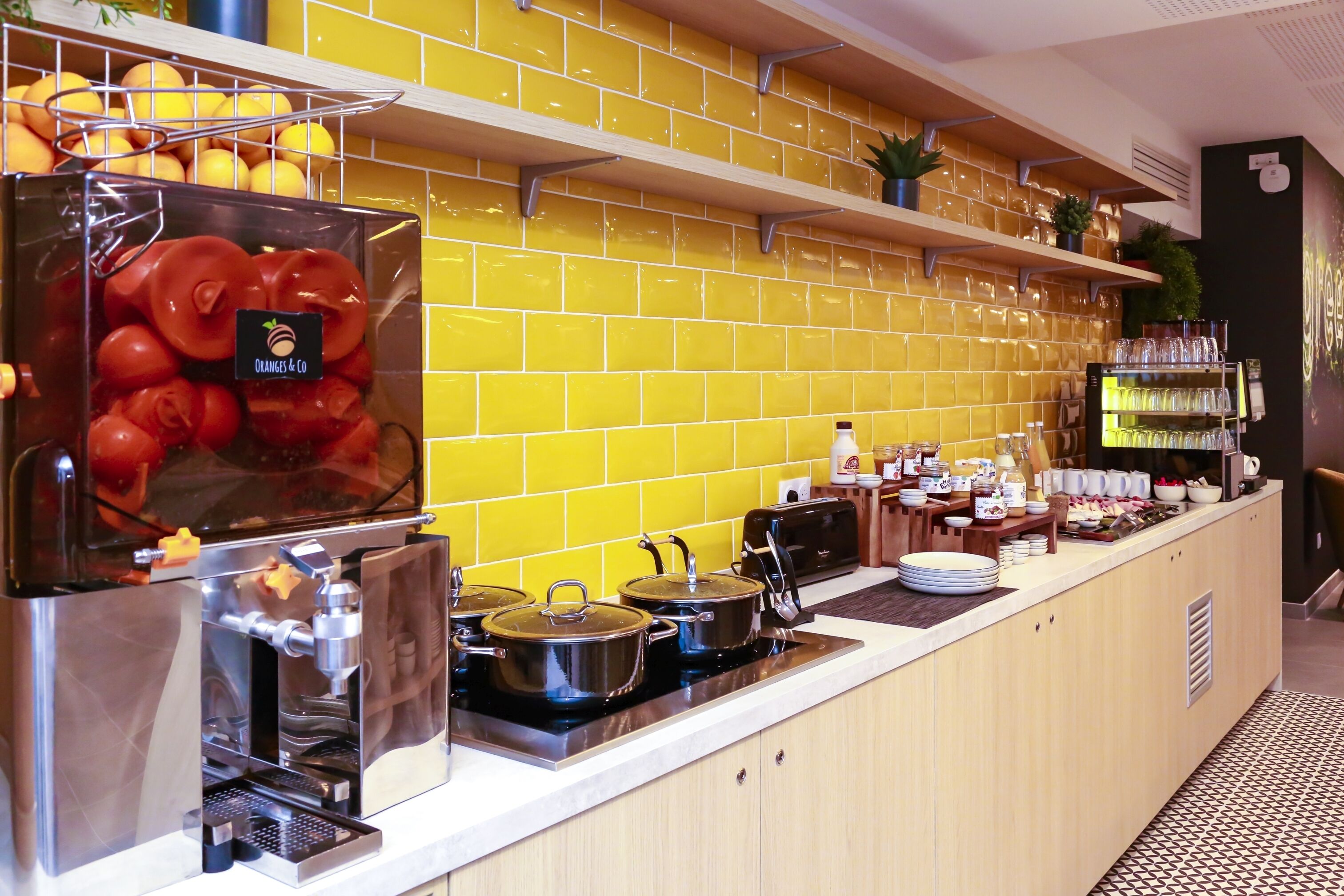 A kitchen with a yellow-tiled backsplash, a coffee machine, and a fruit display.