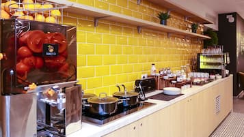 A kitchen with a yellow-tiled backsplash, a coffee machine, and a fruit display.