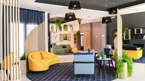 A modern interior with a yellow sofa, a blue patterned ottoman, and a black and white patterned rug. - Appart Hotel Odalys City Angers Centre Gare (Angers)