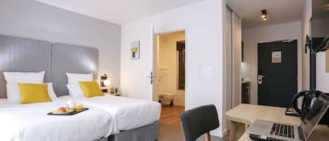 A hotel room with a bed, a desk with a laptop, a chair, and a breakfast tray.