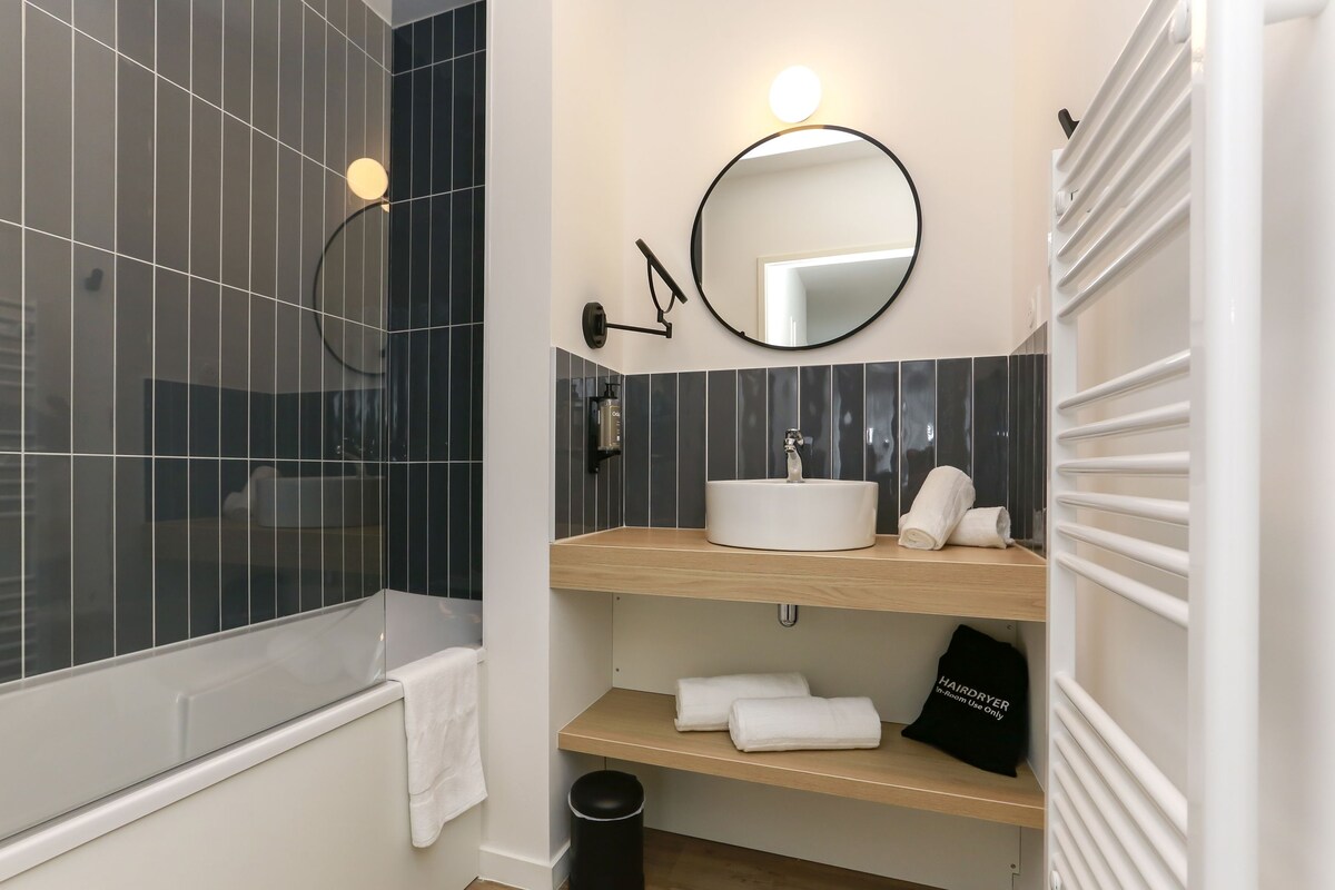 Un baño moderno con bañera, un lavamanos con espejo y un perchero para toallas.