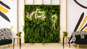 A room with a green wall decorated with ferns and a neon sign that reads "Garden Party". There are two black and white patterned chairs and small tables with potted plants. - Appart Hotel Odalys City Angers Centre Gare (Angers)