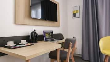 Ein Hotelzimmer mit einem Holztisch, einem Laptop, einer Kaffeemaschine, einem Fernseher und einem Stuhl.