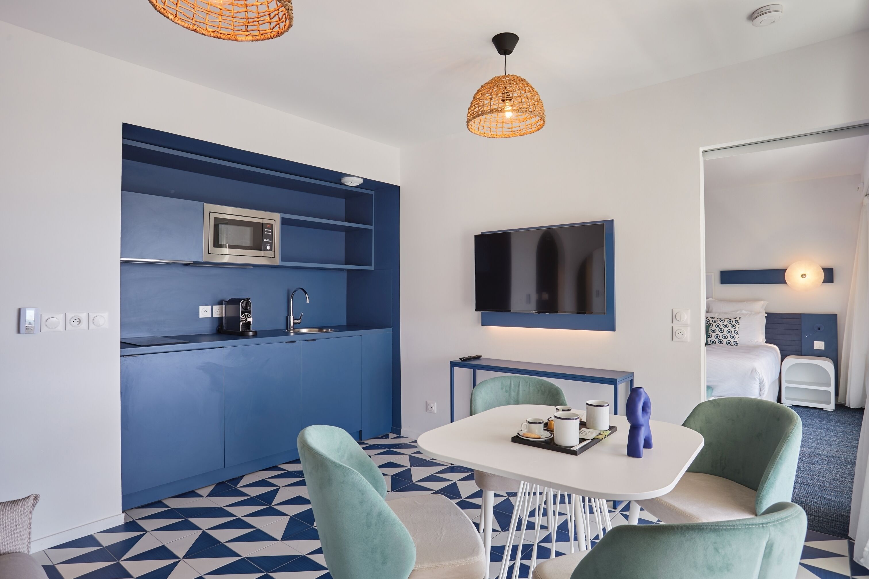 A modern kitchenette with a microwave, sink, and a flat-screen TV mounted on the wall.
