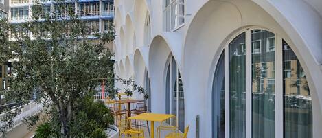 A modern hotel with a courtyard featuring yellow tables and chairs, surrounded by white arches and large windows.