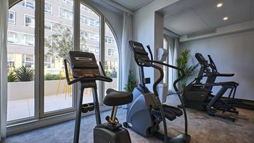 A gym with treadmills, an elliptical, and a stationary bike, large windows, and a view of a building outside.