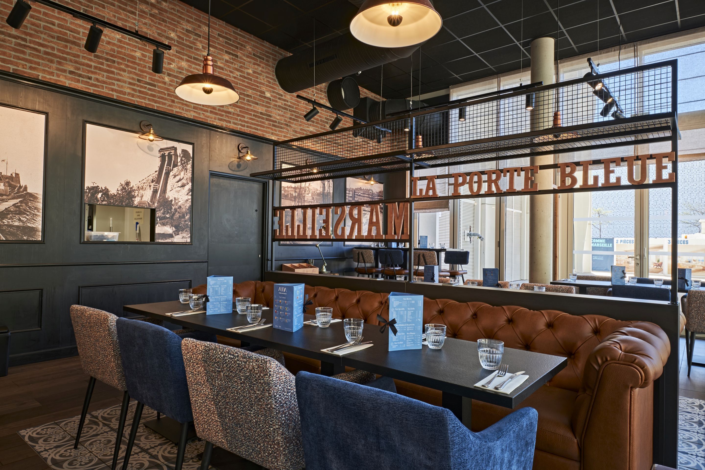 A restaurant with a long table, cushioned seating, and large windows offering a city view.