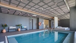 An indoor swimming pool with a modern ceiling design, seating area with cushions, and a lifebuoy on the wall. - Appart Hotel Odalys City Marseille Centre Euromed (Marseille)
