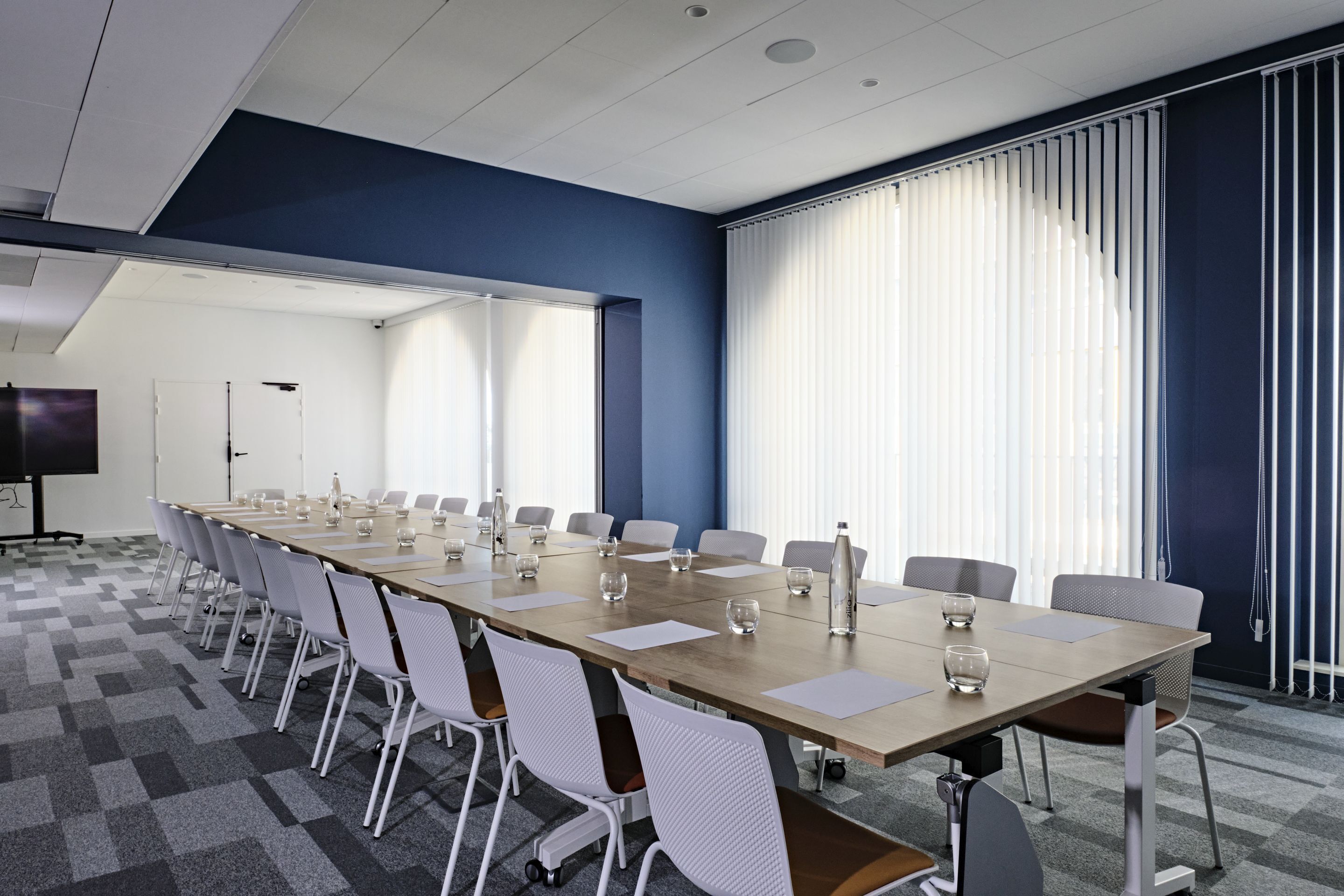 A conference room with a long table, chairs, and a projector screen.