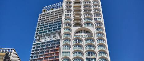A tall building with a modern architectural design, featuring multiple balconies and a distinctive arched window pattern.