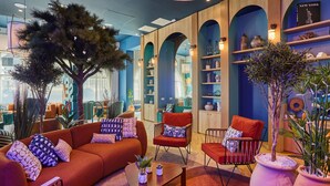 A modern interior with a red sofa, a wooden chair, and a coffee table. There are shelves with decorative items and a large tree in the center. - Appart Hotel Odalys City Marseille Centre Euromed (Marseille)