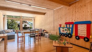 A wooden-floored room with a sofa, chairs, a table, and a play area with toys. - Holzboxen Planneralm (Irdning-Donnersbachtal)