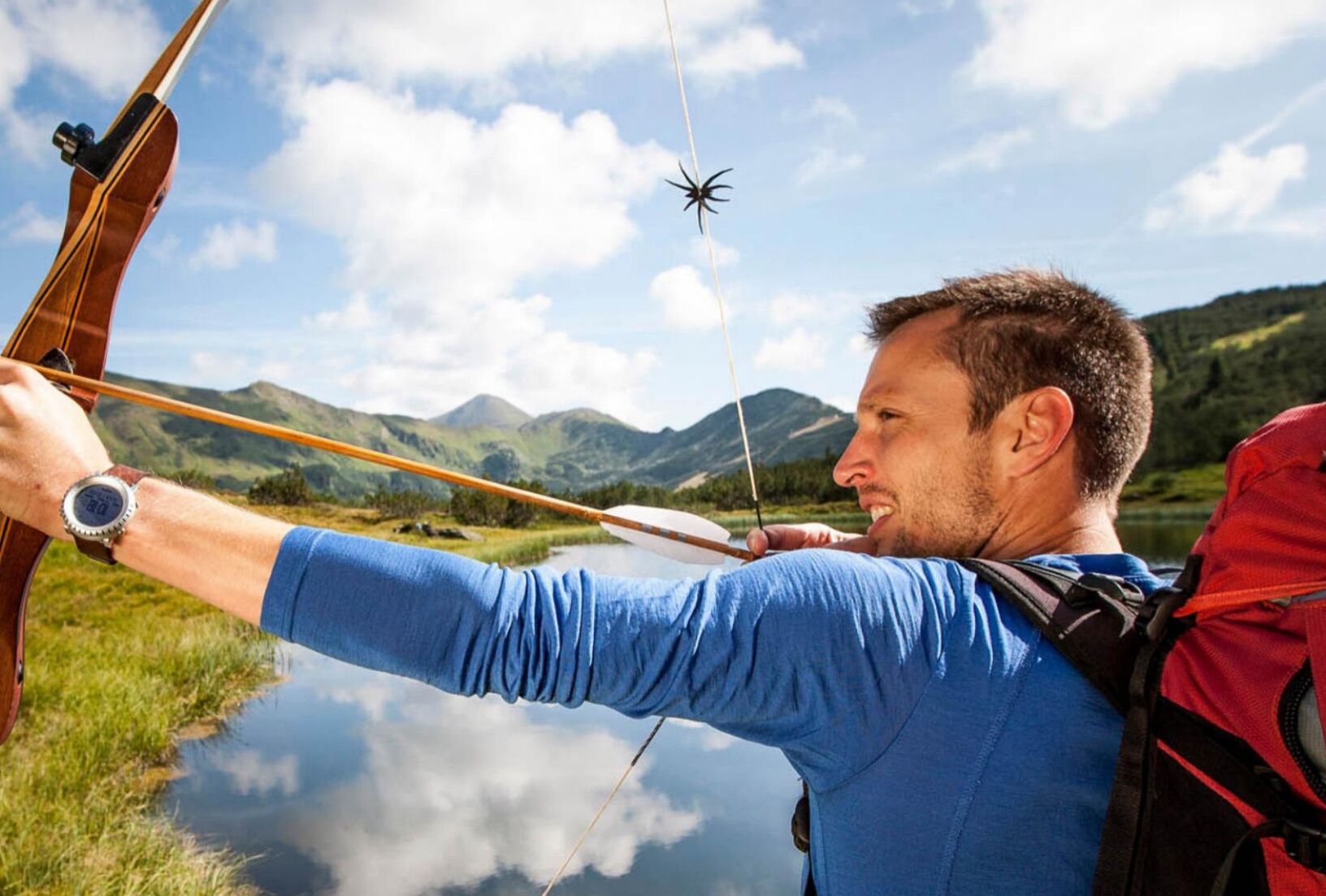 A person aiming a bow with a natural landscape in the background.