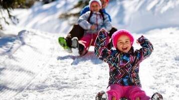 A snowy landscape with a sled being pulled by a child in a colorful jacket and pink hat.