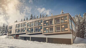 A modern building with multiple windows and a flat roof, surrounded by snow-covered trees. - Holzboxen Planneralm (Irdning-Donnersbachtal)
