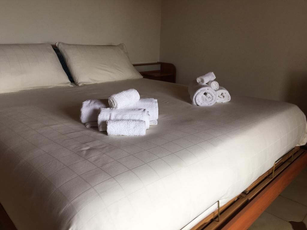 Een net opgemaakt bed met opgerolde witte handdoeken en een stapel handdoeken ernaast.