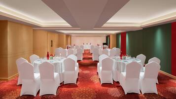 Un salón de conferencias con mesas redondas y sillas blancas, una alfombra de diseño rojo y una decoración en tonos neutros.