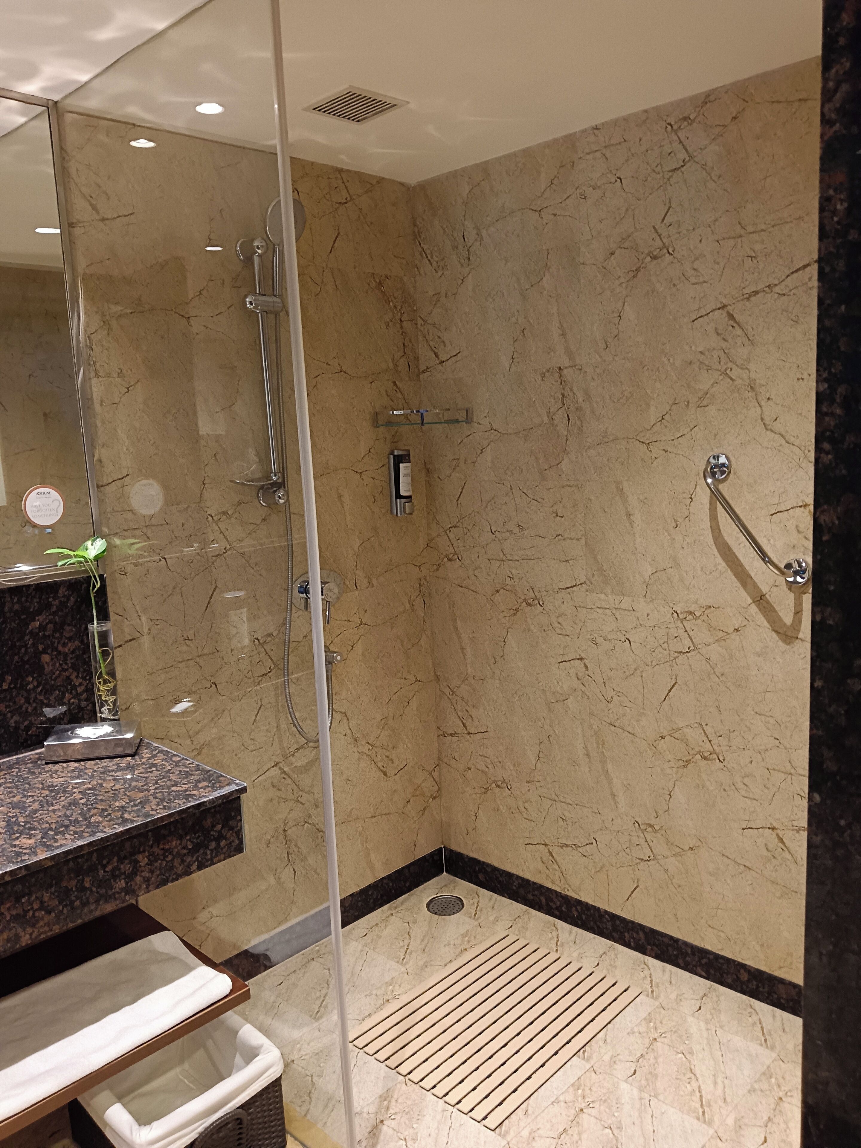 A modern bathroom with a glass-enclosed shower, marble walls, and a granite countertop.