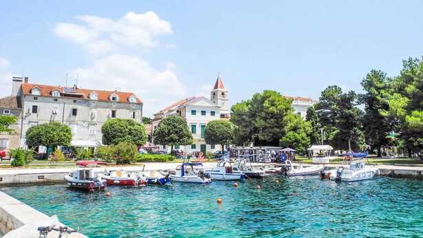 A waterfront area with boats docked, buildings with red-tiled roofs, and a clock tower.
