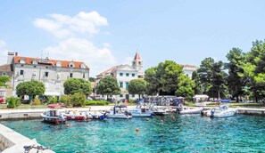 A waterfront area with boats docked, buildings with red-tiled roofs, and a clock tower.