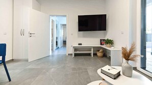 A modern living room with a flat-screen TV, a white cabinet, a bench, and a vase with dried plants.