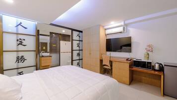 A hotel room with a bed, a desk, a chair, a microwave, a refrigerator, and a TV.