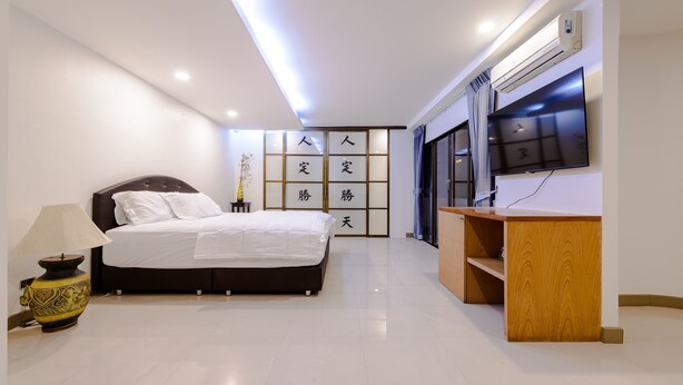 A modern bedroom with a bed, bedside table, lamp, and a TV mounted on the wall. - Pasadena Lodge (Pattaya)
