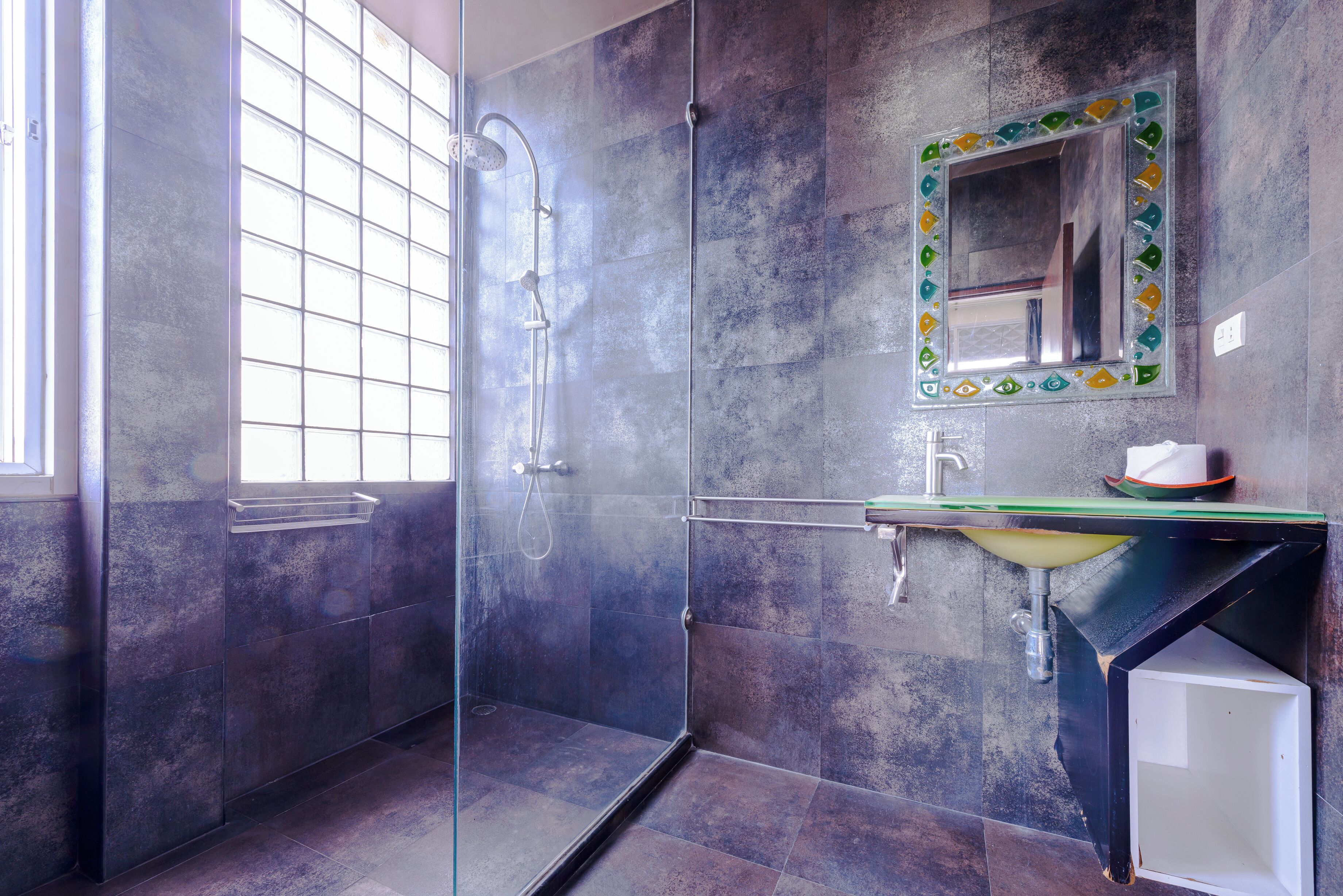 Ein modernes Badezimmer mit einer gläsernen Duschkabine, einem Waschbecken mit grüner Arbeitsplatte und einem Spiegel mit dekorativem Rahmen.