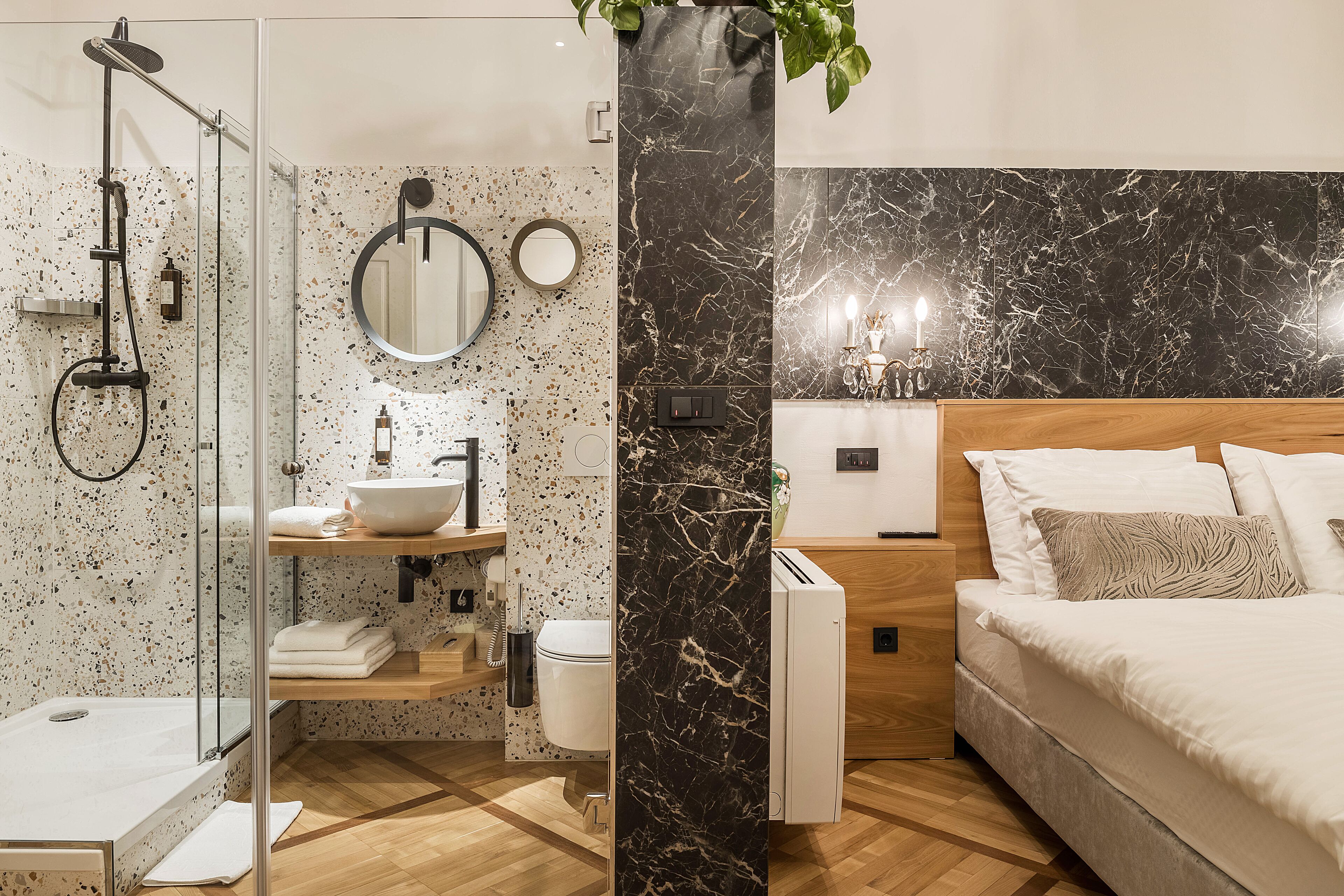 Een moderne badkamer met douche, toilet en wastafel, en een slaapkamer met een bed en nachtkastje.