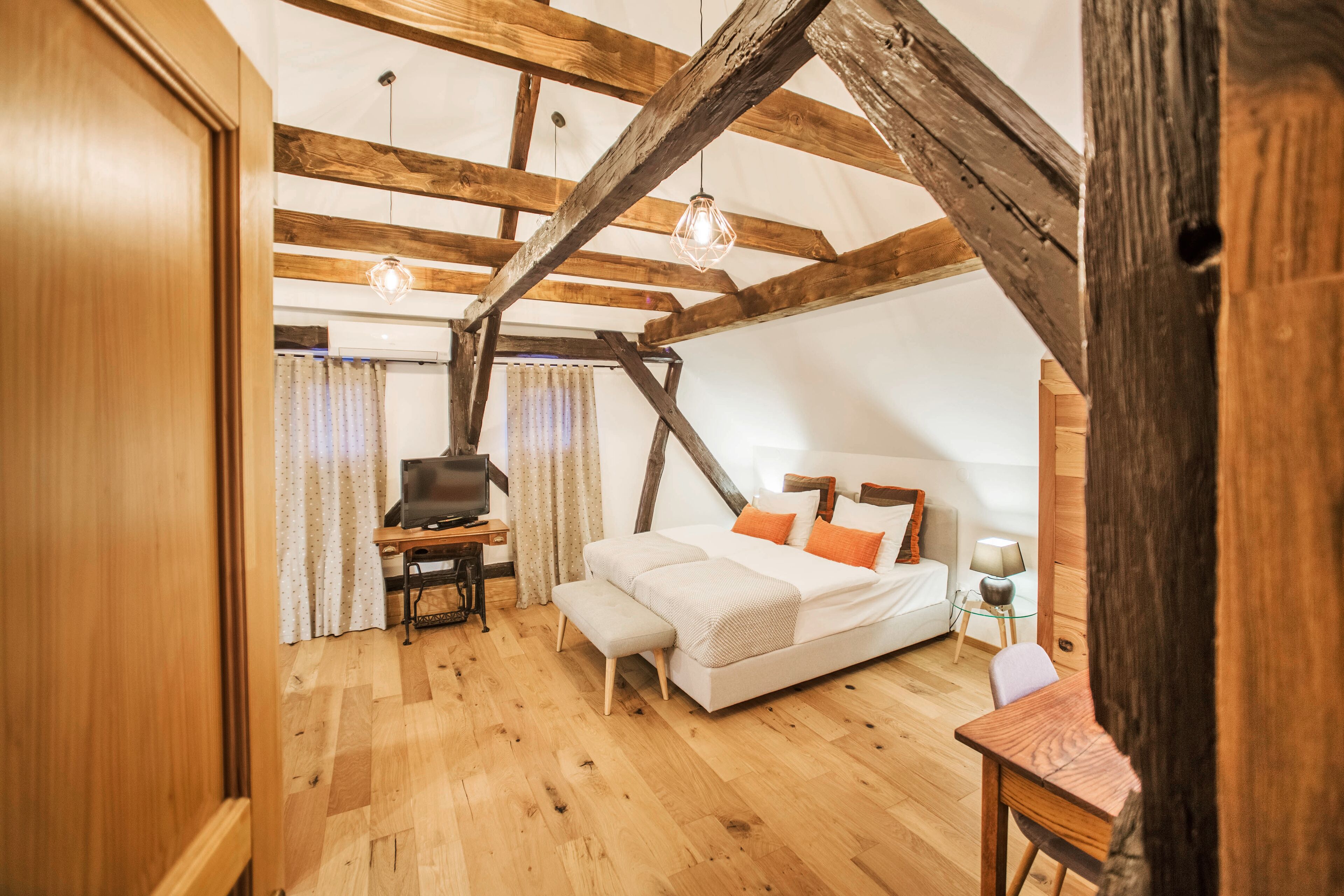 A bedroom with a wooden ceiling, a bed, a desk, and a TV.